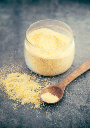 Yellow corn flour in a glass jar on a rustic table. Ingredients for preparation of a Italian traditional Polenta, porridge made from cornmeal. Organic food.の写真素材