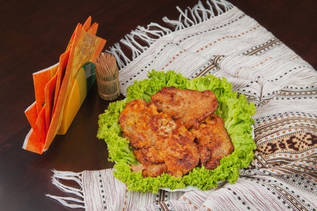 There are cutlets on the plate decorated with lettuce, napkins and wooden sticks on the dark brown table with cover.の写真素材