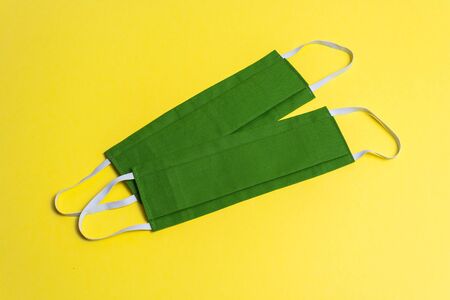 Two colored reusable medical masks on a yellow background, isolated. Green hygiene, antiviral, protective, handmade masks close-up, top view, for prophylaxis against coronavirus, covid-19の写真素材