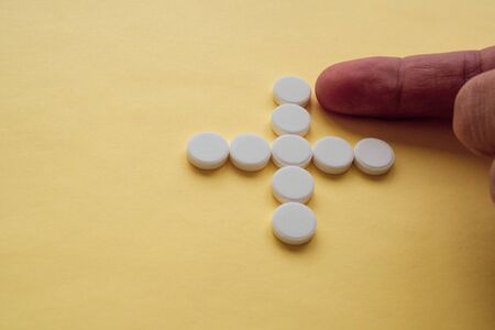 round white tablets in the shape of a cross on a yellow background, tablets are located in the center, with a finger pointing to itの写真素材