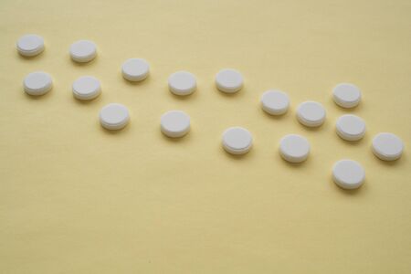 round white color pills on a yellow background,  tablets are arranged in a row throughout the image