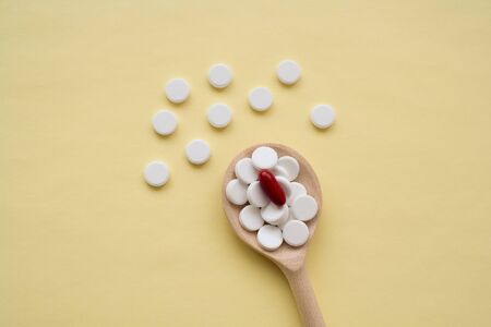 round white tablets with one red capsule on a wooden spoon on a yellow background, tablets are...