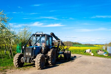 Modern tractor closeup in village against the background of rape field, forest blue sky....