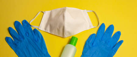 Protective equipment kit against pandemic, coronavirus closeup, top view. Medical, hygiene face mask, antiseptic in bottle and blue gloves on yellow background, isolated Banner for web siteの写真素材