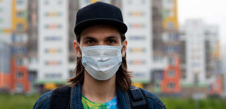 Handsome young man in regular disposable surgical, medical mask on the street in the city. Coronavirus, covid-19 protection. Banner for web site. Portrait made in front closeupの写真素材