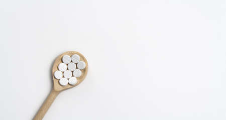 Wooden spoon with round tablets on white background isolated on the left side. Medications on the...
