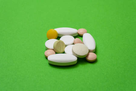 Bunch colorful round pills and capsules on a green background close up, macroshot tablets, isolated....