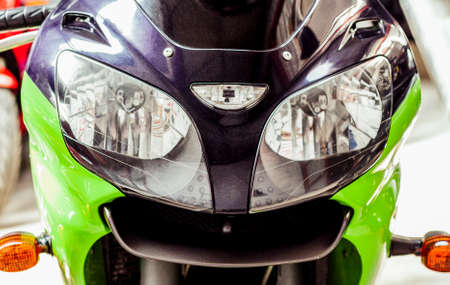Pair headlights front view of motorcycle in showroom close up. Glossy green-black windproof shield with turn signals of sportbike. Front part of modern motorcycle in salon, with handlebarの写真素材