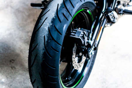 Rear wheel of sports motorcycle with green-black cast disc, close-up. Running gear, suspension, motorcycle tire, brake discs, support. Road fast motorcycle in the garage for repair, maintenance.の写真素材