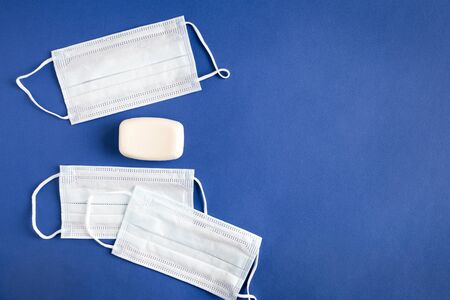 Few isolated objects on a blue paper background with copy space. Three face mask protection against flu, pollution, virus and coronavirus. Next to it is a piece of white hand soap.の写真素材