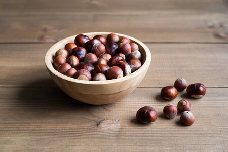 Hazelnuts and chestnuts lie in a wooden bowl, which stands on a wooden background of boards. A few nuts are lying next to the bowl.の写真素材