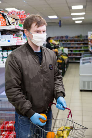 Moscow, Russia April 04, 2020: Young man buys products in a supermarket during Coronavirus pandemic. On him wearing a mask and rubber gloves that protect him against infection, viruses and COVID-19.のeditorial素材