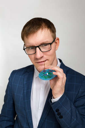 A waist-high portrait of a handsome young man in modern glasses holding a small cocktail umbrella and looking at the camera. He is wearing casual clothing, a jacket and shirt. He looked thoughtful and interested.の写真素材