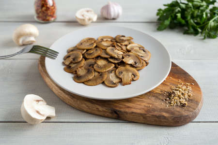 Appetizer of roasted slices mushrooms on a light plate on a wooden stand. Healthy vegetarian food close up on a white wooden backgroundの写真素材
