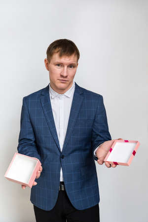 Young man with short dark hair and no beard in a casual suit is holding an open, empty gift box. On his face the disappointment and bewilderment. Portrait on a white background.の写真素材