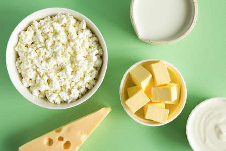 Most common products from milk are butter, cheese, milk, sour cream, cottage cheese on a green paper background flat lay. Natural, organic food. Foods for strong bonesの写真素材