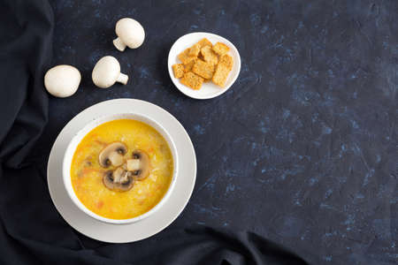 Champignon soup in a white bowl on dark textile. Top of the soup is decorated with slices of sliced mushroom. Flat lay with place for text on dark blue backgroundの写真素材