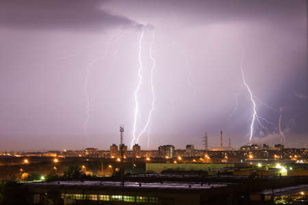 Powerful lightning strike hits the city at night. A strong lightning strike over a dark gray sky hits the ground, illuminating the town.の写真素材