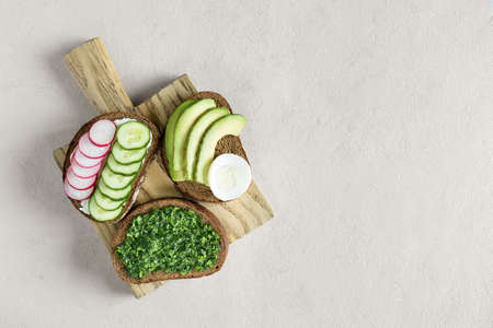 Various homemade sandwiches with radish, pesto, cucumber and cheese on the gray background. Slices of vegetables on bread. Healthy snack. Flat lay, top view, place for text.の写真素材
