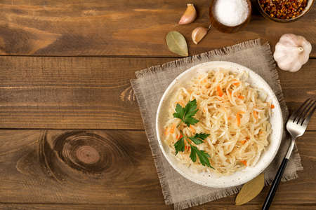 White ceramic plate with homemade appetizer sauerkraut decorated parsley on brown wooden background flat lay with copy space. Next to salt, garlic and bay leafの写真素材