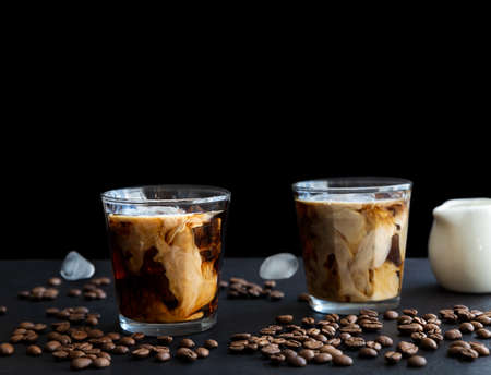 Two glass iced coffee with cream, ice cubes and coffee beans on dark background with copy space. Refreshing drinkの写真素材
