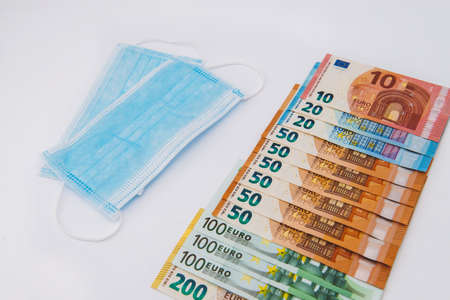 Medical face mask and euro on white background. Face mask with euro banknotes. Financial crisis. Concept of business related to the purchase and sale of masks against coronavirus Covid-19の写真素材