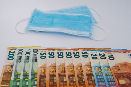 Medical face mask and euro on white background. Face mask with euro banknotes. Financial crisis. Concept of business related to the purchase and sale of masks against coronavirus Covid-19の写真素材