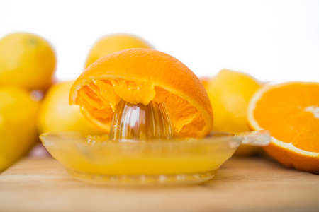 On a wooden board he squeezes fresh oranges with a juicer. Orange juice in a glass close to half of sliced ââoranges on a white background.の写真素材
