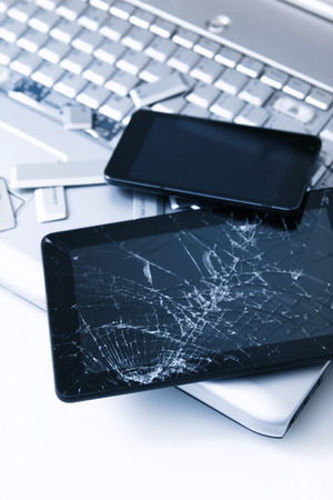 A silver laptop with a broken keyboard, tablet with a cracked display and black phone. A close-up picture of part of broken laptop and cracked screen on a tablet.の写真素材