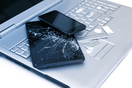 A silver laptop with a broken keyboard, tablet with a cracked display and black phone. A close-up picture of part of broken laptop and cracked screen on a tablet.の写真素材