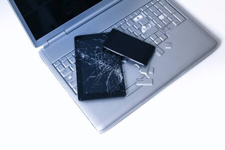 A silver laptop with a broken keyboard, tablet with a cracked display and black phone. A close-up picture of part of broken laptop and cracked screen on a tablet.の写真素材