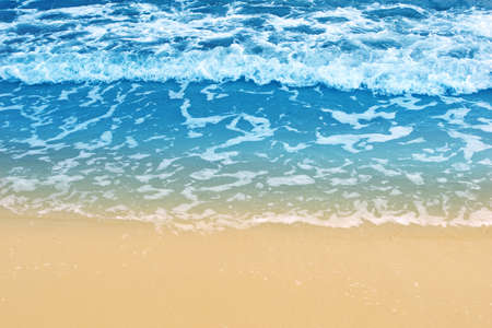 Soft wave of blue ocean on sandy beach. Background. Empty beach with sea foam washing up from sea. の写真素材