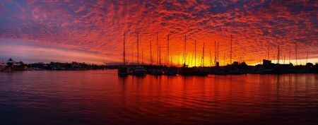Quite an unusual mix of colors in this tropical sunset over a Mooloolaba marina,Queensland -Australia The masts of Yachts are in silhouette against a sunset through clouds.の写真素材