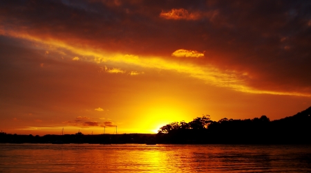 Orange Blaze - Strikingly beautiful golden sunset over water through cloud and trees with bright water reflections,の写真素材