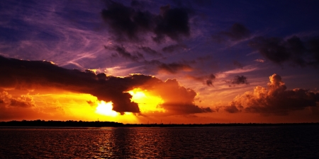  Vibrant multicolored striking sunset  Strong colors ranging from white yellow gold black and pale blue over ocean and with back llit cloud and some water reflections の写真素材