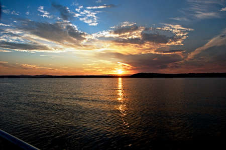Vivid gold clouds and blue sky sunset seascape cloudscape with water reflections in the tranquil waters of Lake Macquarie at dusk.の写真素材