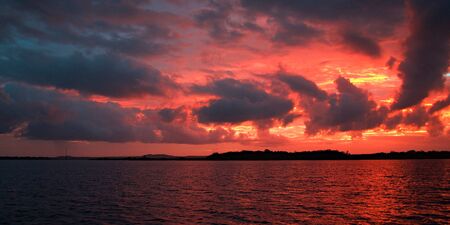 Vivid crimson and yellow cloudy ocean sunset with dark backlit clouds and water reflections.Photograph was taken off the Australian  East Coast.の写真素材