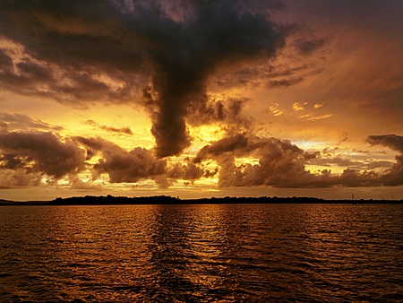 Vivid orange and yellow cloudy ocean sunset with dark backlit clouds and water reflections.Photograph was taken off the Australian  East Coast.の写真素材