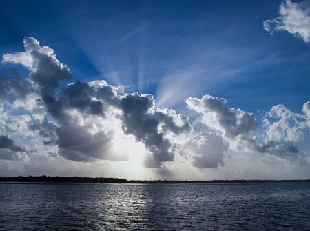 A spectacular inspirational brightly coloured cloudy sea water tropical seascape featuring a billowing white Cumulus cloud formation and clear Crepuscular Rays in a mid blue sky with ocean water reflections, Australia.の写真素材