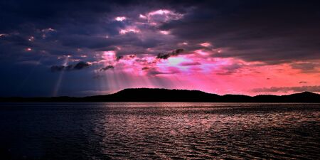 Delightful inspirational brightly coloured cloudy sea water panoramic sunrise seascape featuring distinctave crepuscular rays with ocean water reflections. Port Stephens, Australia.の写真素材