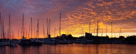A vivid orange marina sunrise with water reflections and boats in silhouette. An absolutly stunning end to a most enjoyable nautical day. Queensland,Australia.の写真素材