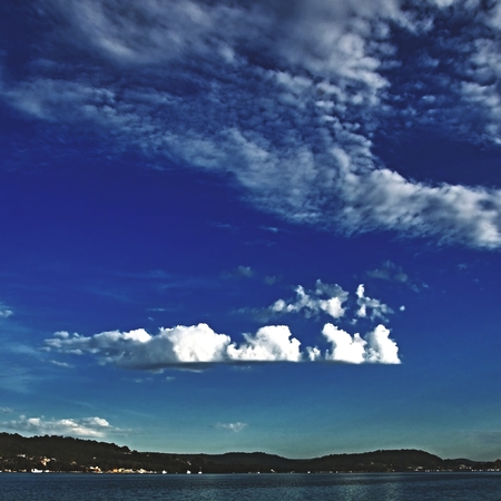 A spectacular inspirational brightly coloured cloudy sea water tropical seascape featuring billowing white Cumulus and Cirrus cloud formation in a mid blue sky with ocean water reflections. Australia.の写真素材