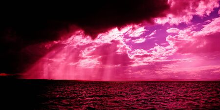 A spectacular hot pink sunbeams sunrise over tropical water with brightly colored crepuscular rays and colorful sea water ocean reflections. Queensland, Australia.の写真素材