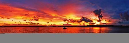 A spectacular inspirational brightly coloured cloudy sea water tropical panoramic sunrise seascape featuring silhouettes with ocean water reflections. Queensland, Australia.の写真素材