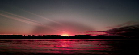 A spectacular inspirational brightly coloured red and grey cloudy sea water tropical panoramic sunrise seascape featuring silhouettes with ocean water reflections. Queensland, Australia.の写真素材