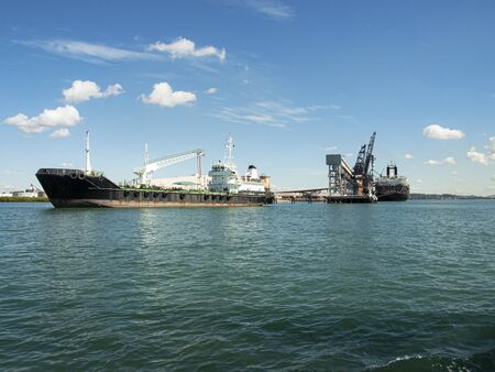 Ships berthed at the coal loader terminal Port Gladstone in tropical water with blue sky backdrop. Queensland, Australia.の写真素材