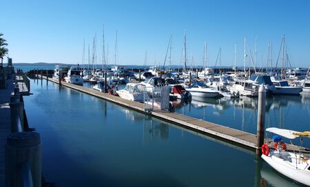 Picturesque Marina. Waterfront walkway with boats in tropical water with blue sky backdrop. Safe haven for sailing and cruising vessels.  Urungan Marina, Queensland, Australia.の写真素材