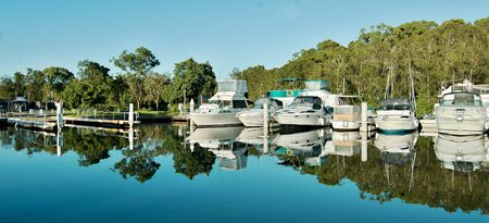 Water reflections at a country marina/dock with boats in tropical water with blue sky backdrop. Bush setting for sailing and cruising vessels. Lake Macquarie, Australia.の写真素材