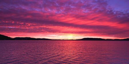 A magnificient panoramic inspirational magenta coloured altostratus cloudy sunrise seascape over sea water with water reflections. Gosford, New South Wales, Australia.の写真素材