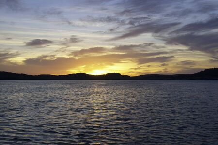 A striking inspirational gold coloured stratocumulus cloudy coastal sunrise seascape over sea water with water reflections. Gosford, New South Wales, Australia.の写真素材